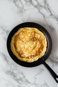 cooking-thin-crepes-in-black-skillet-on-white-marble
