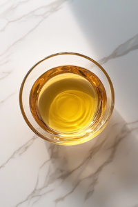 This image shows a small glass bowl filled with melted golden butter resting on a clean white marble cooktop.
