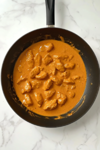 creamy-butter-chicken-sauce-reducing-in-black-skillet-with-one-handle-on-white-marble