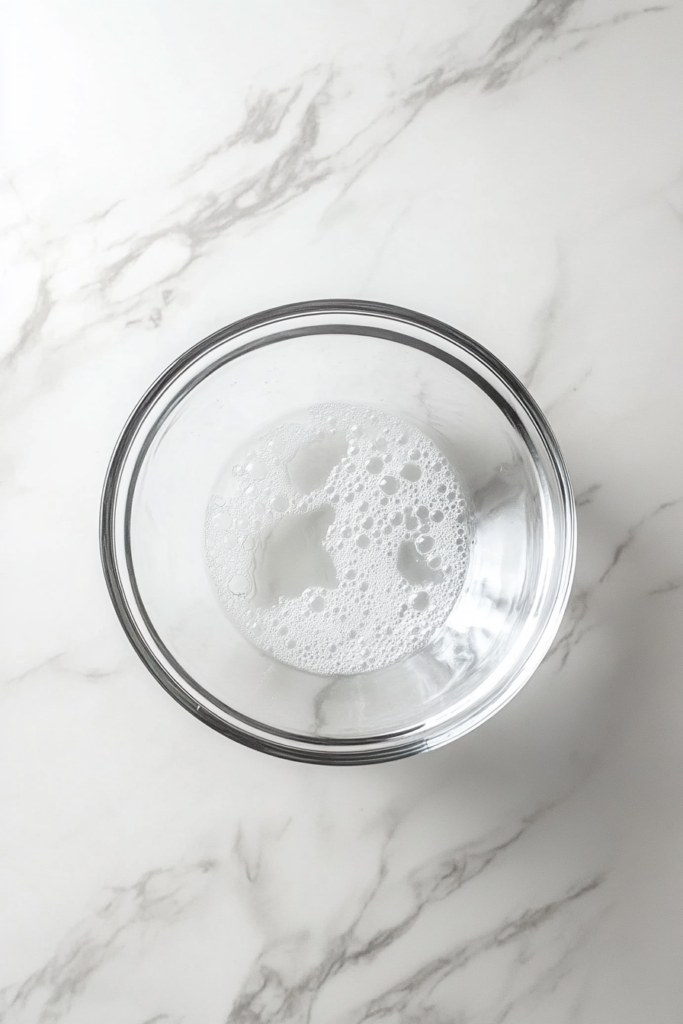 dissolving-yeast-and-sugar-in-warm-water-in-clear-glass-bowl-on-marble-9277038-683x1024