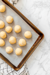 This image shows a top-down view of cookies baking in the oven on parchment-lined trays over a white marble countertop.