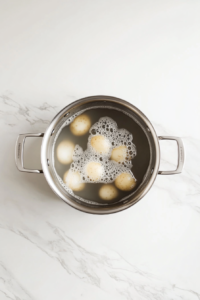 This image shows diced potatoes simmering in water in a stainless steel pot on a clean white marble countertop.