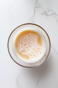 This image shows stiffly whipped egg whites in a clean glass bowl, viewed from the top on a white marble counter.
