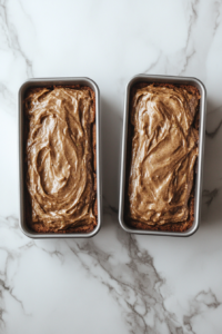This image shows two 8x4-inch loaf pans filled with zucchini banana bread batter, placed on a white marble countertop.
