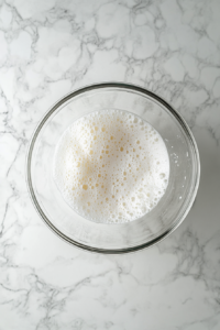 frothy-egg-whites-in-glass-bowl-before-sugar-addition-on-white-marble