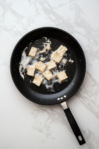 frying-tofu-until-golden-in-black-skillet-vegan-fried-chicken