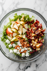 This image shows a fully tossed Autumn Chopped Salad in a glass bowl, placed on a white marble cooktop with all ingredients evenly coated.