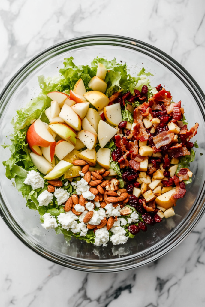 This image shows a fully tossed Autumn Chopped Salad in a glass bowl, placed on a white marble cooktop with all ingredients evenly coated.