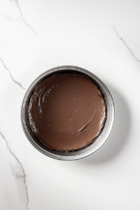 This image shows a cake tin filled with smooth Gateau Au Chocolat batter, ready for baking, placed on a white marble countertop.