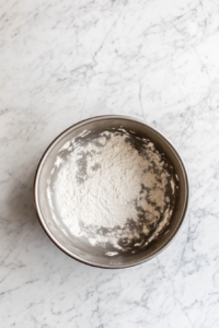This image shows diced apples tossed with sugar and cinnamon in a clear glass bowl on a white marble countertop.