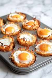 This image shows the cooked egg and hash brown baskets in a muffin tin placed on a white marble countertop, with the edges loosened and a few baskets gently popped out.