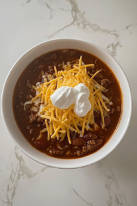 homemade-chili-served-with-shredded-cheese-and-sour-cream-on-white-marble-countertop