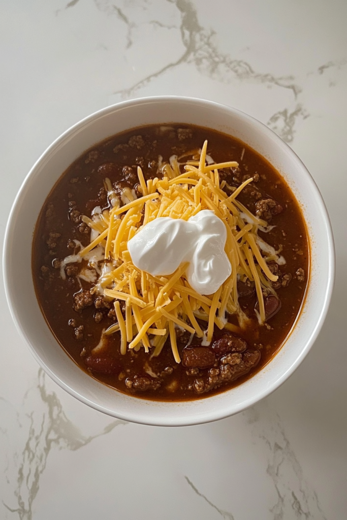 homemade-chili-served-with-shredded-cheese-and-sour-cream-on-white-marble-countertop