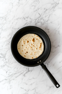 lavash-bread-cooking-in-black-non-stick-skillet-on-white-marble