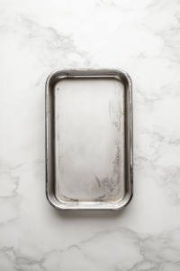 This image shows a clean metal loaf pan evenly coated with baking spray, sitting on a white marble countertop.