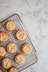 This image shows a top-down view of warm Earl Grey cookies on a tray, with a round metal cutter placed around one cookie to shape it on a white marble countertop