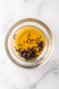 This image shows a top-down view of a glass bowl with melted butter and Earl Grey tea leaves on a white marble countertop.