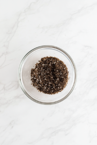 This image shows a top-down view of a glass bowl with melted butter, Earl Grey tea, granulated sugar, and brown sugar mixed together on a white marble countertop.