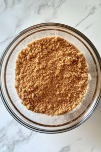 This image shows dry ingredients including flour, cornmeal, sugar, baking powder, baking soda, salt, and cinnamon in a clear glass bowl on a white marble countertop.