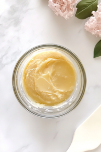 This image shows a glass bowl on a white marble countertop with butter-sugar mixture, vanilla, salt, and flour being combined into a crumbly cookie dough.