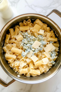 pouring-blue-cheese-dressing-and-milk-into-cheesy-rigatoni-in-stainless-steel-pot