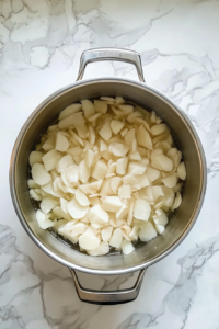 This image shows a stainless steel pot filled with water and raw diced potatoes on a white marble countertop.