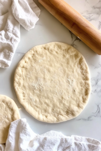 rolled-dough-disc-next-to-wooden-rolling-pin-on-floured-marble