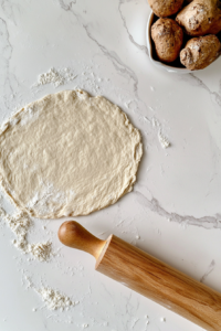 This image shows the dough rolled out paper-thin on a floured white marble surface, with a wooden rolling pin beside it.