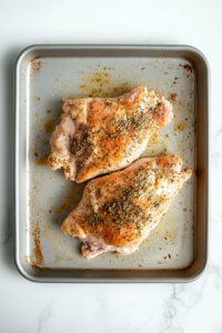 seasoned-chicken-chest-on-baking-sheet-over-white-marble