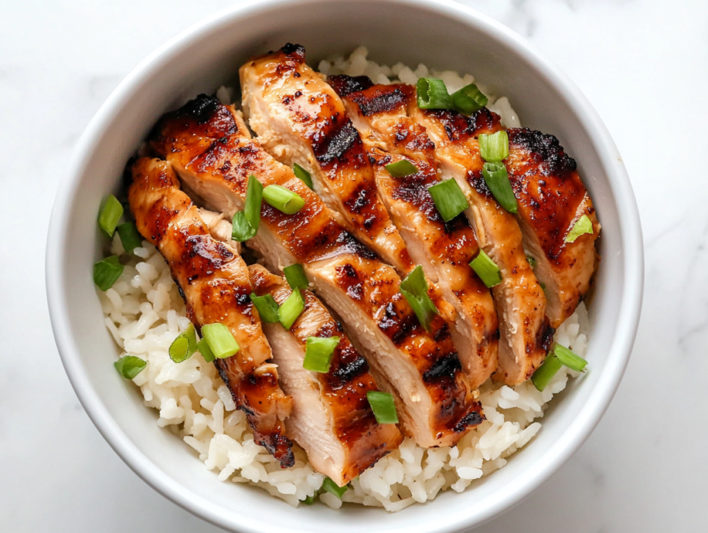 This image shows a bowl of Hawaiian grilled chicken served over coconut rice on a white marble countertop, with clean, minimal presentation and golden grilled textures.