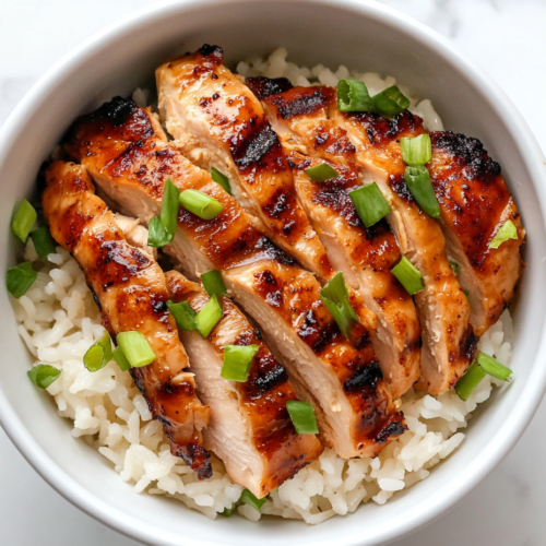 This image shows a bowl of Hawaiian grilled chicken served over coconut rice on a white marble countertop, with clean, minimal presentation and golden grilled textures.