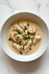 serving-keto-crockpot-chicken-alfredo-served-in-ceramic-white-bowl-on-marble