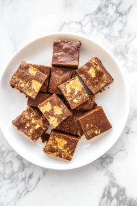 This image shows a top-down view of baked peanut butter brownies cooling in a glass dish placed on a white marble cooktop before slicing.