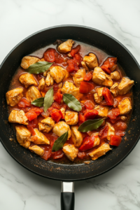 simmering-chicken-tomato-mixture-low-heat-black-skillet-white-marble