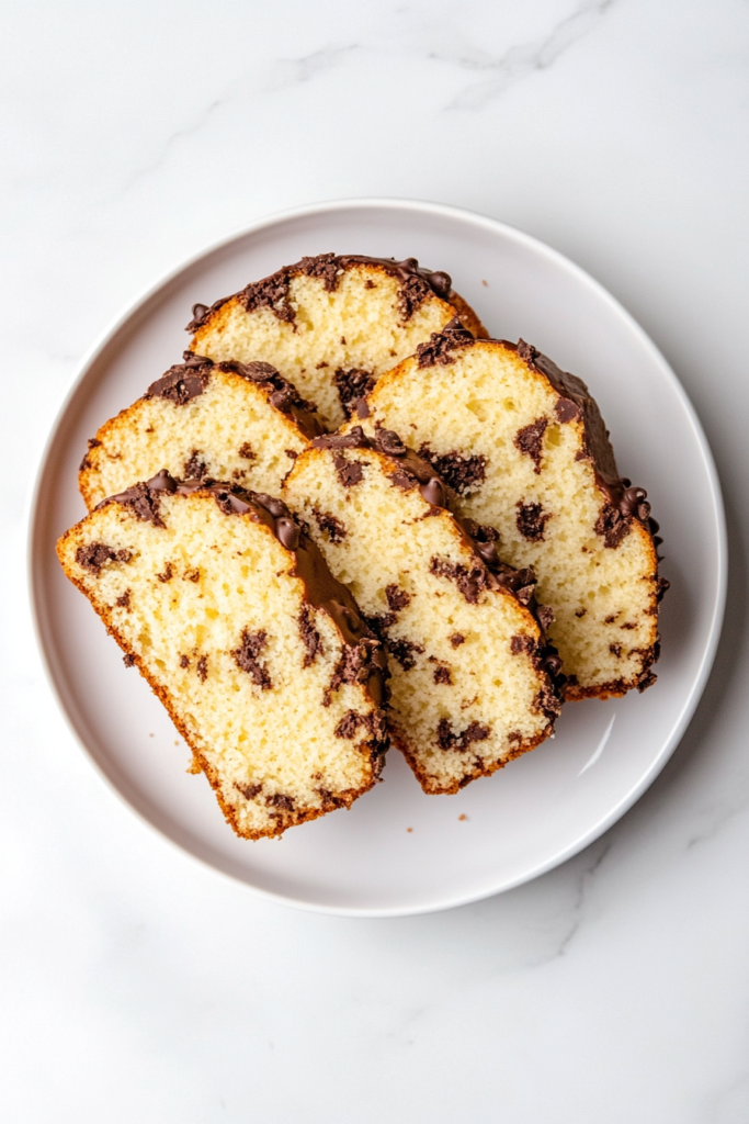 This image shows freshly baked chocolate chip pound cake slices arranged neatly on a white ceramic plate placed over a white marble countertop.