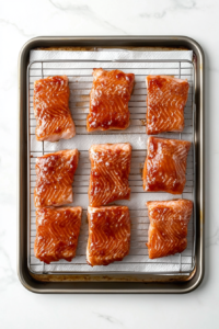 This image shows lightly oiled salmon fillets skin-side down on a black smoker rack, with the smoker set to low heat, on a white marble countertop.