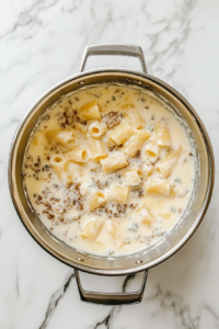 stirring-blue-cheese-dressing-and-milk-into-rigatoni-in-stainless-steel-pot