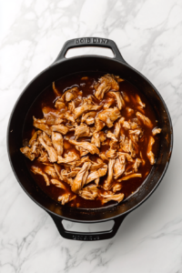stirring-shredded-chicken-into-sauce-in-black-dutch-oven-on-marble