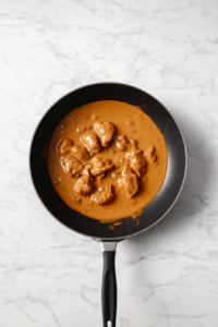 tikka-chicken-simmering-in-creamy-skillet-sauce-on-white-marble