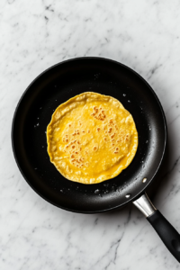 This image shows a single corn tortilla warming in a black nonstick skillet over a white marble cooktop, slightly puffed and aromatic.