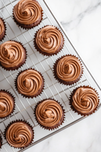 This image shows a mini cupcake pan with each liner two-thirds full of vanilla batter, placed on a spotless white marble countertop.