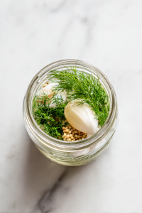 adding-aromatics-garlic-mustard-seeds-dill-to-mason-jar-for-pickled-cherry-tomatoes