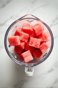 adding-chopped-watermelon-to-glass-blender-on-white-marble