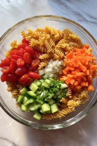adding-cooked-pasta-to-veggie-bowl-on-white-marble