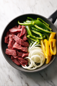 adding-steak-peppers-onions-to-skillet