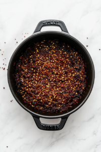 black-dutch-oven-cooking-tomato-paste-red-pepper-oregano-on-white-marble
