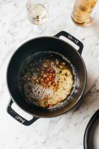 black-dutch-oven-reducing-white-wine-with-tomato-mixture-on-white-marble