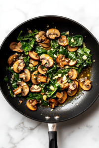 black-nonstick-skillet-sauteing-spinach-mushrooms-garlic-white-marble