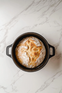 bread-baking-on-stovetop-in-black-dutch-oven-on-white-marble