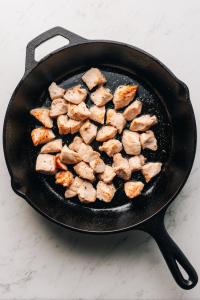 browned-chicken-pieces-in-black-skillet-on-white-marble